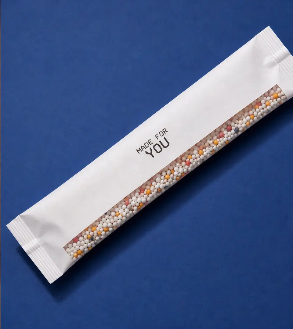 Personalised supplement sachet filled with colourful microgranules on a cobalt blue background